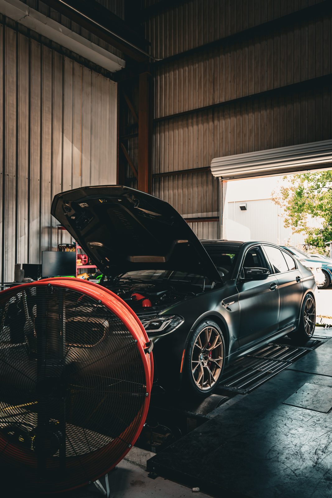 Matte black BMW M5 with the hood open inside the Cruz Automotive service bay